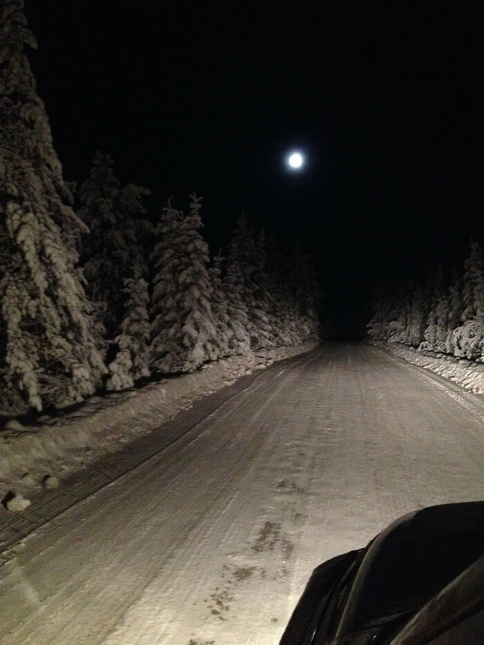 Snow-covered road at night with a full moon, illustrating creepy and unsettling worker photos for jobs that should pay more.