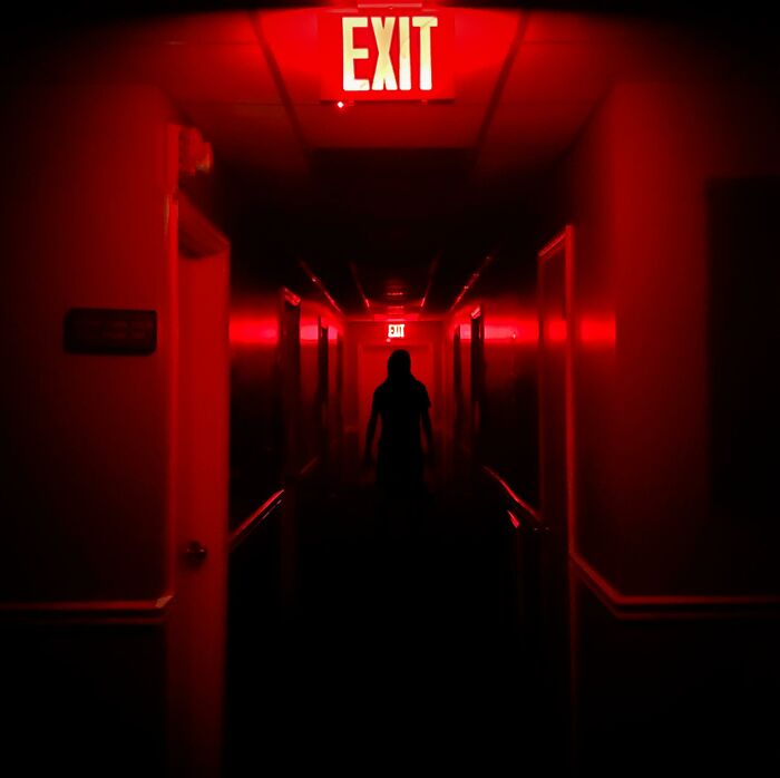 Creepy and unsettling photo of a dark hallway with a shadowy figure under a glowing exit sign, highlighting jobs that should pay more.