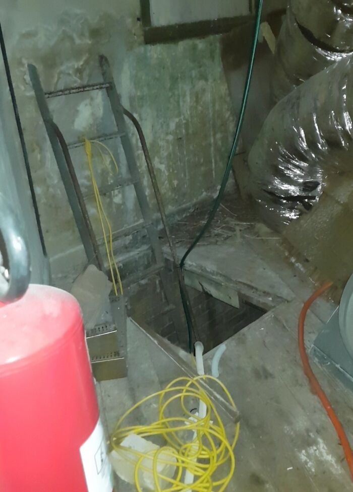 Creepy and unsettling photo of a cramped work space with exposed wiring and a ladder leading to a dark hole.