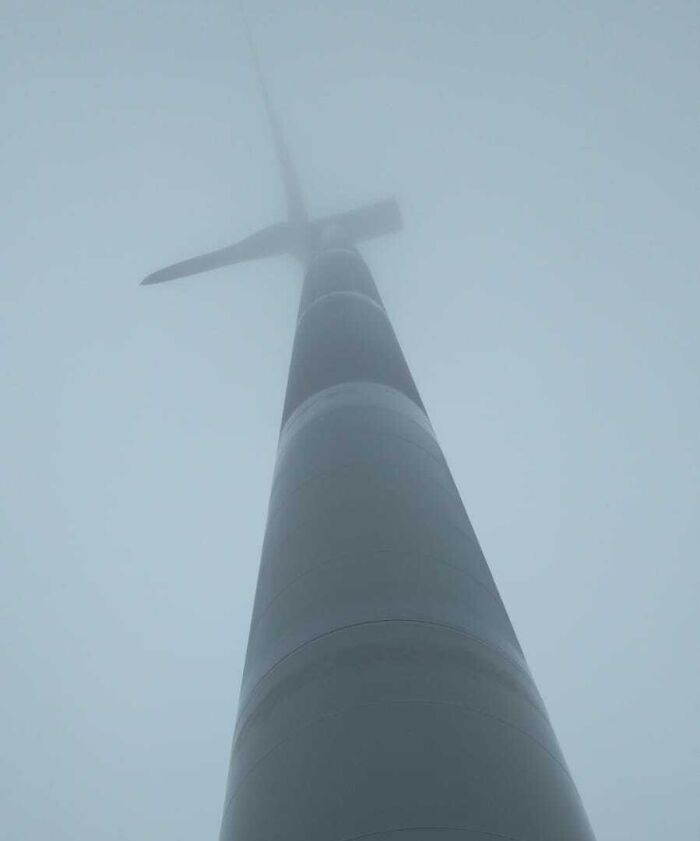 Wind turbine towering into foggy sky, an unsettling photo highlighting jobs that should pay more for challenging conditions.