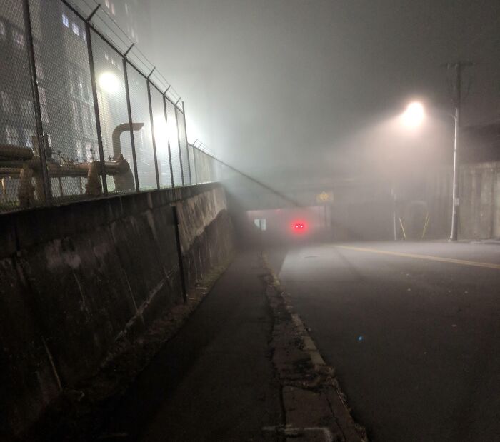 Foggy nighttime street with a dimly lit sidewalk and fence, illustrating unsettling photos taken by workers.