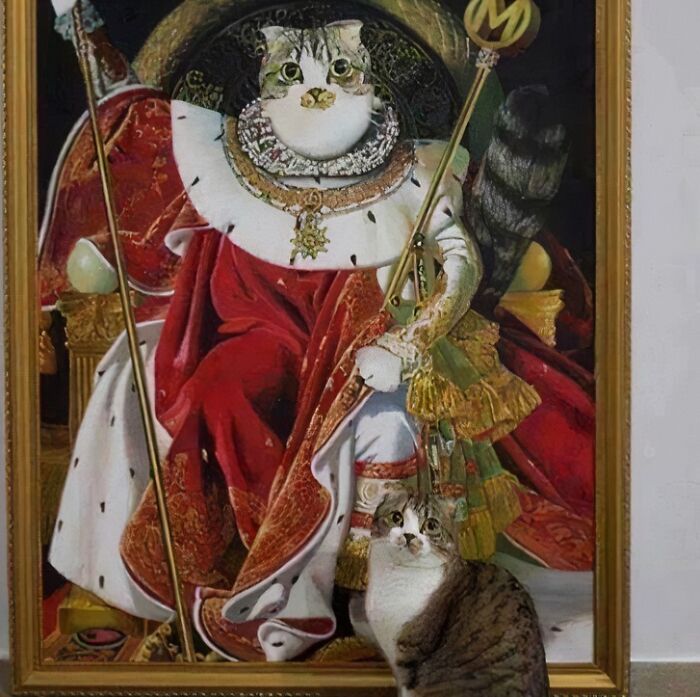 Cat posing in front of a medieval-style portrait showing medieval cats dressed in royal attire with a crown and scepter.