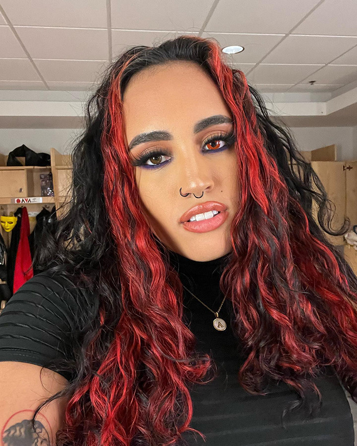 The Rock's daughter with red and black hair, wearing a black top and necklace, posing indoors with bold makeup. The Rock's daughter with red and black hair, wearing a black top and necklace, posing indoors with bold makeup.