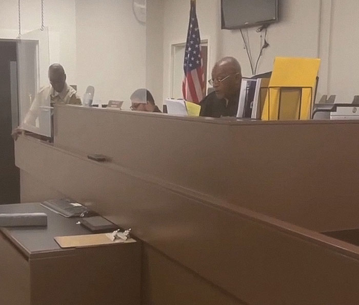 Courtroom scene with officials discussing the case of a teacher arrested for using poop spray around school. Courtroom scene with officials discussing the case of a teacher arrested for using poop spray around school.