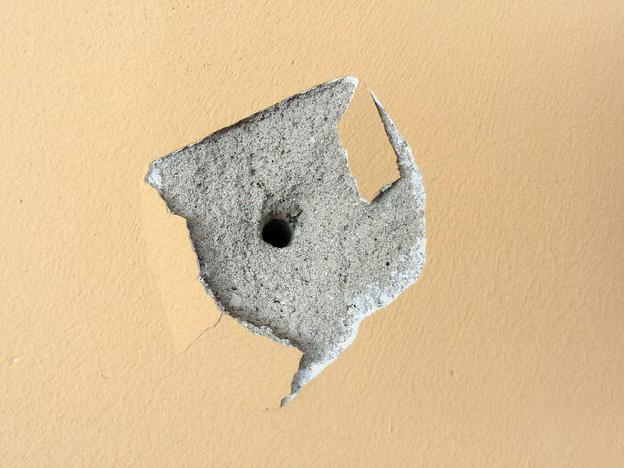 Close-up of a damaged wall showing exposed concrete and a hole, illustrating nasty things exes did that shocked partners.