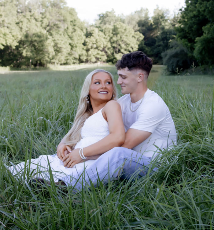 Cheerleader appearing all glammed up in court, sitting outdoors with partner in a grassy field, smiling and embracing. Cheerleader appearing all glammed up in court, sitting outdoors with partner in a grassy field, smiling and embracing.