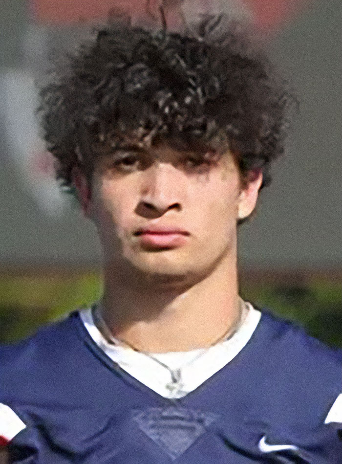 Young man with curly hair in a blue sports jersey, posing outdoors with a serious expression and blurred background. Young man with curly hair in a blue sports jersey, posing outdoors with a serious expression and blurred background.