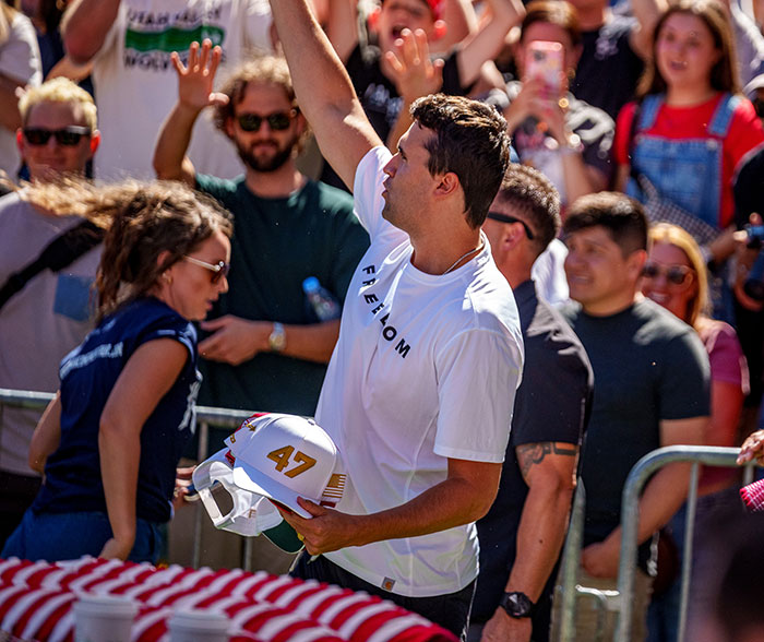 Man in a white freedom shirt holding a hat with number 47 at a crowded outdoor event with people cheering and raising hands. Man in a white freedom shirt holding a hat with number 47 at a crowded outdoor event with people cheering and raising hands.
