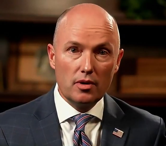 Man in suit with an American flag pin, serious expression, representing FBI revealing DNA evidence in Tyler Robinson case. Man in suit with an American flag pin, serious expression, representing FBI revealing DNA evidence in Tyler Robinson case.