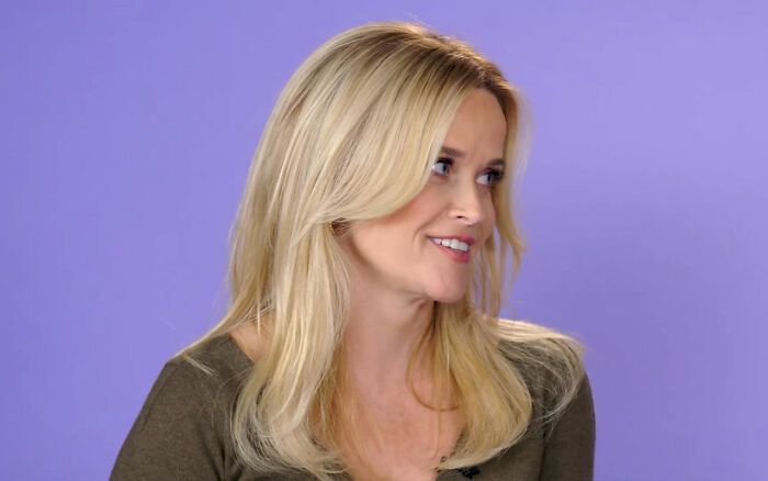 Blonde woman smiling and looking to the side against a purple background in a Jennifer Aniston Reese Witherspoon context. Blonde woman smiling and looking to the side against a purple background in a Jennifer Aniston Reese Witherspoon context.