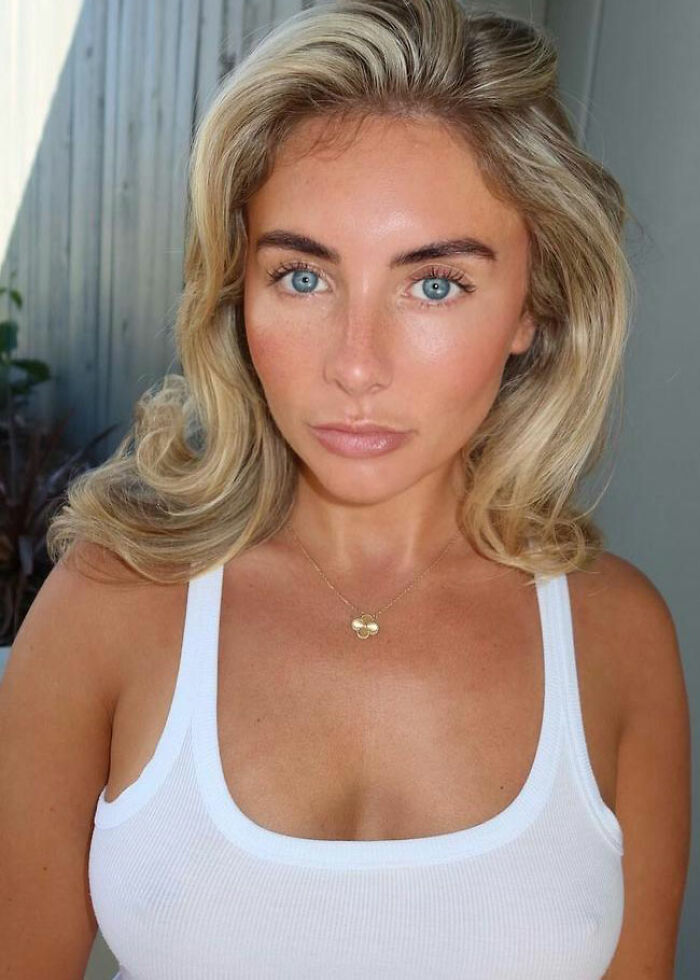 Adult star Bonnie Blue with blonde hair and blue eyes wearing a white tank top in a casual indoor setting. Adult star Bonnie Blue with blonde hair and blue eyes wearing a white tank top in a casual indoor setting.