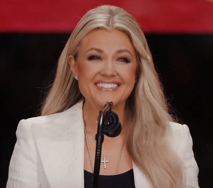 Woman with long blonde hair smiling at a microphone during an event with WWE level stuff discussed by netizens. Woman with long blonde hair smiling at a microphone during an event with WWE level stuff discussed by netizens.