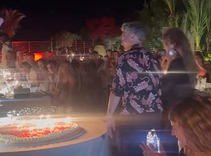 Sacha Baron Cohen at a nighttime party with a large cake, surrounded by guests celebrating at an outdoor event. Sacha Baron Cohen at a nighttime party with a large cake, surrounded by guests celebrating at an outdoor event.