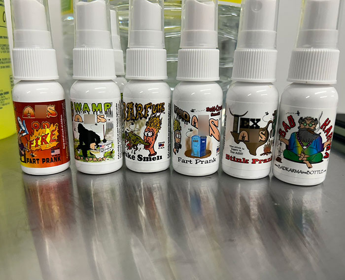 Several small prank spray bottles labeled with fart and stink prank themes displayed on a metal surface. Several small prank spray bottles labeled with fart and stink prank themes displayed on a metal surface.