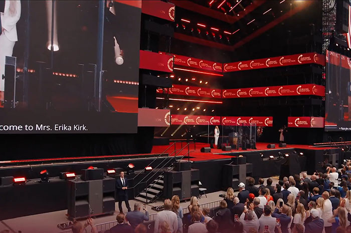 Crowd watching a large stage event with multiple screens featuring Erika Kirk's surprising entrance at a memorial ceremony. Crowd watching a large stage event with multiple screens featuring Erika Kirk's surprising entrance at a memorial ceremony.
