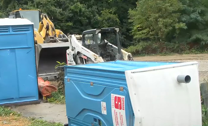 Blue porta-potty tipped over near construction equipment in an outdoor area, related to cop shooting teens over porta-potty prank. Blue porta-potty tipped over near construction equipment in an outdoor area, related to cop shooting teens over porta-potty prank.