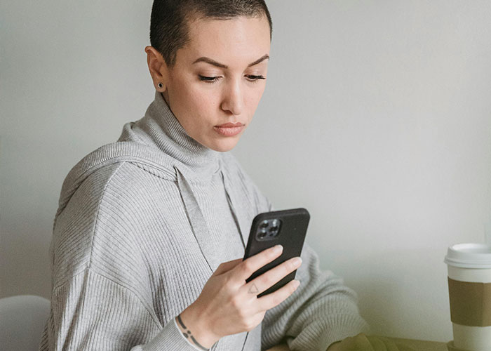 Woman at home looking serious while holding a phone, relating to shutting down brother’s proposal at baby shower. Woman at home looking serious while holding a phone, relating to shutting down brother’s proposal at baby shower.
