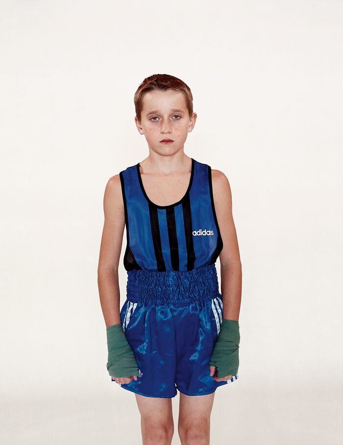 Young boxer standing in blue Adidas boxing outfit with hand wraps before their first match, looking serious and focused.