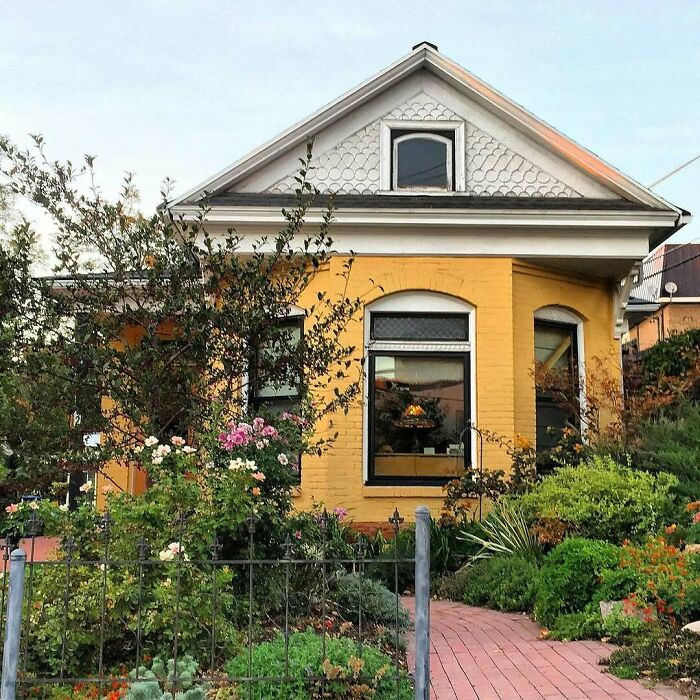Charming old home with a yellow brick exterior surrounded by a lush garden and colorful flowers.