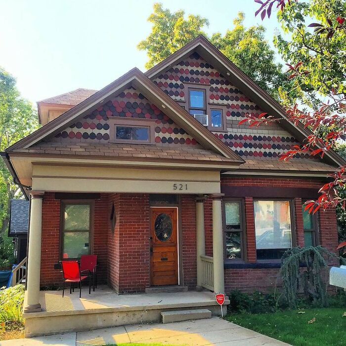 Charming old home with brick facade and decorative shingles, featuring a cozy front porch surrounded by greenery.
