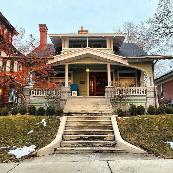 Charming old home with a spacious front porch and steps, surrounded by autumn trees and green lawn.