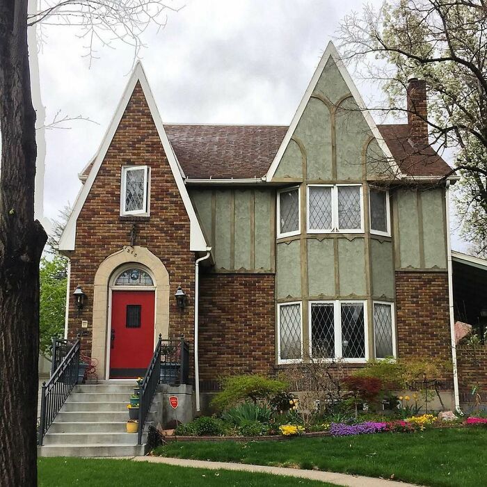 Charming old home with brick and stucco exterior, steep gabled roofs, and a bright red door in a well-kept garden.
