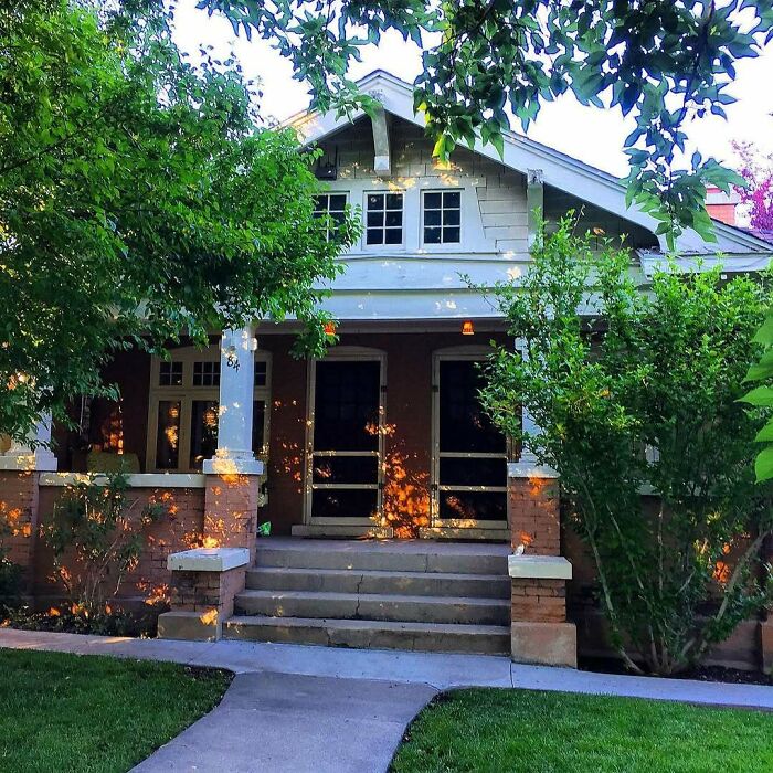 Charming old home with a welcoming front porch surrounded by lush trees and greenery in a sunny neighborhood.