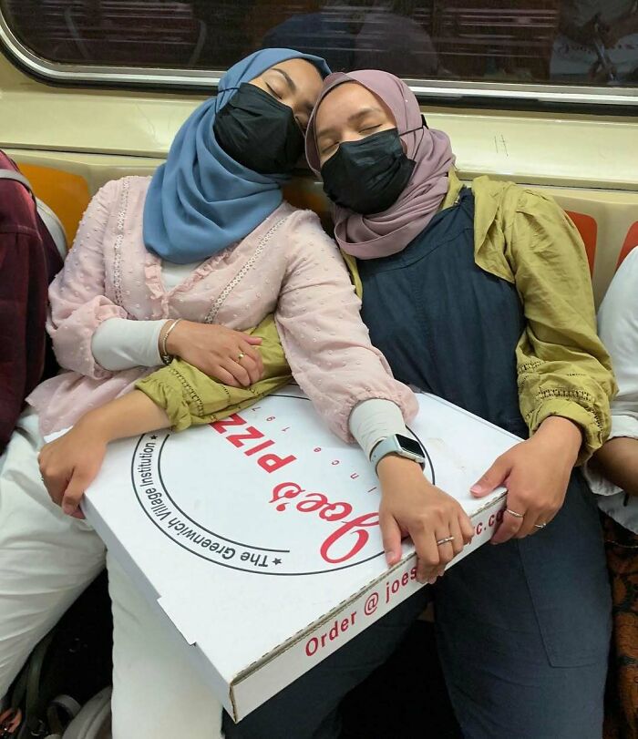 Two women wearing hijabs and masks hold a large pizza box on the New York subway, showcasing unique items passengers carry.