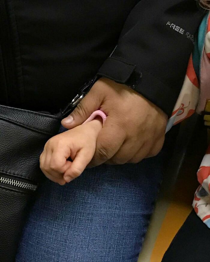 Adult and child holding hands on the New York subway, showcasing one of the cutest things people carry in their hands.