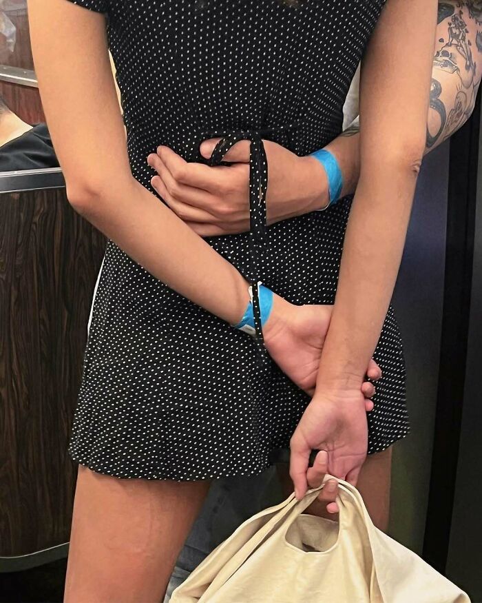 Two people on the New York subway holding hands behind a polka dot dress, one carrying a beige bag.