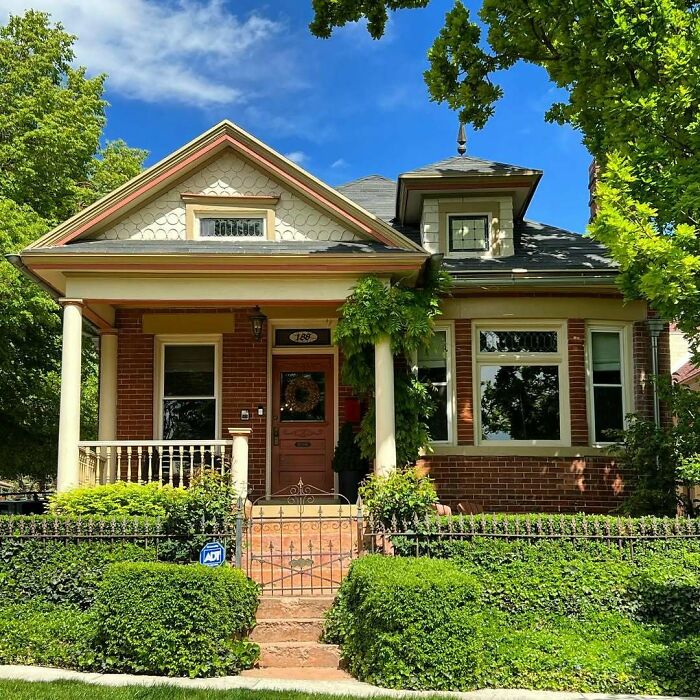 Lovely old home with brick exterior and charming porch surrounded by green trees and hedges on a sunny day