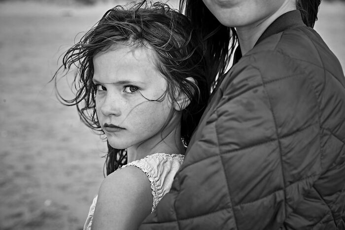 Close-up black-and-white portrait of a serious young girl held by a woman, showcasing award-winning photographic composition.