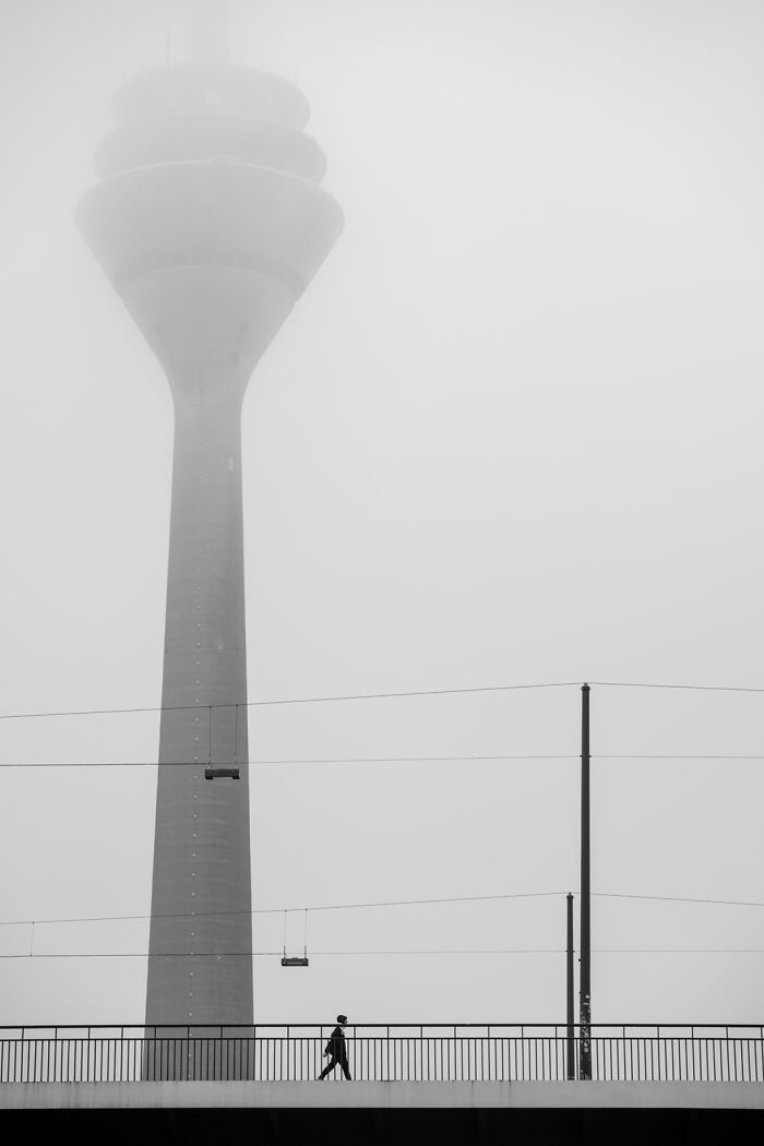 Black and white photo of a person walking on a bridge with a tall tower in the fog from Exposure One Awards