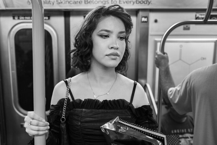 Young woman standing in a subway, holding a pole and notebooks, captured in an award-winning black-and-white photo.