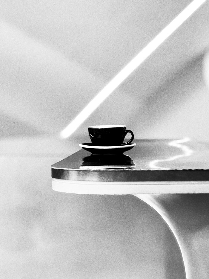 Black-and-white photo of a coffee cup on a table with strong light beams in a minimalistic setting.