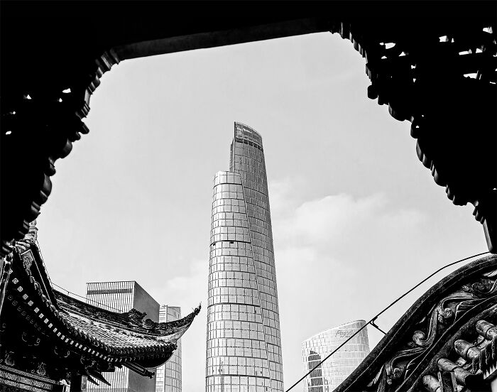 Black-and-white photo of modern skyscraper framed by traditional architecture, showcasing award-winning exposure photography.