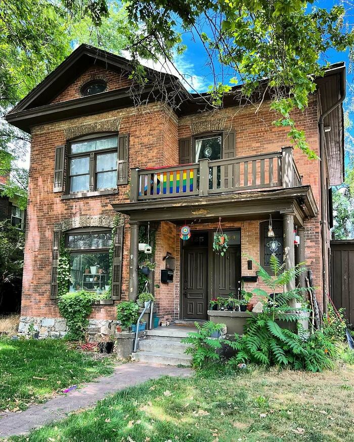 Charming old home with brick exterior, a small front porch, and lush greenery under bright blue sky.