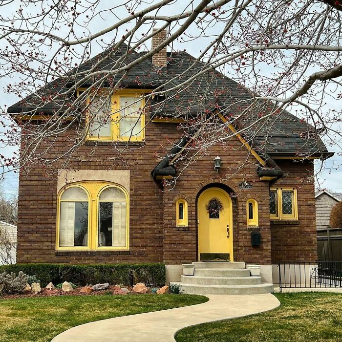 Charming old home with yellow accents, brick facade, and a curved pathway in a peaceful neighborhood setting.