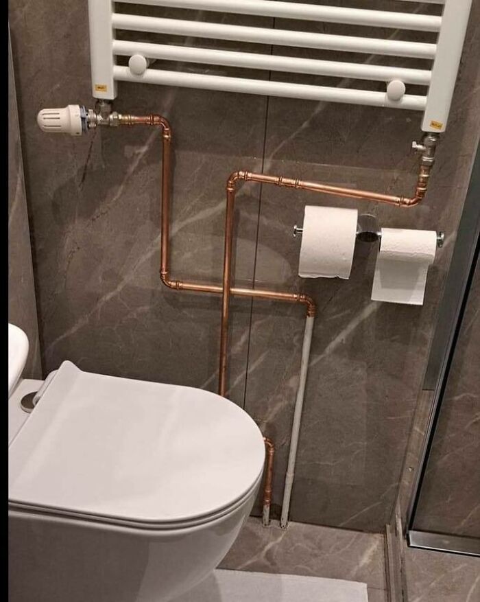 Bathroom plumbing and toilet paper holder made from copper pipes in a construction and design fail.