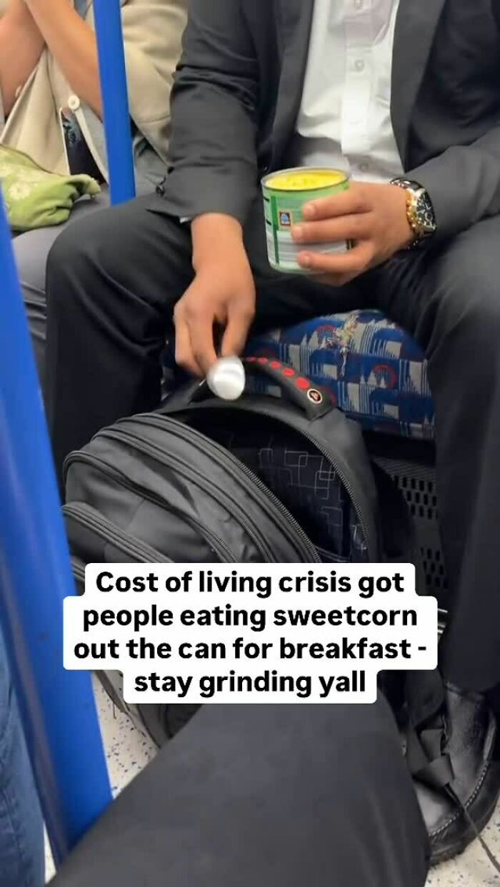 Man in a suit eating sweetcorn from a can on London public transport, reflecting British humor on the cost of living crisis.
