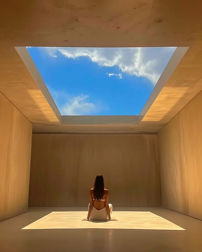 Woman sitting in a minimalist room with a large skylight, sunlight creating a peaceful and dreamy escape atmosphere.