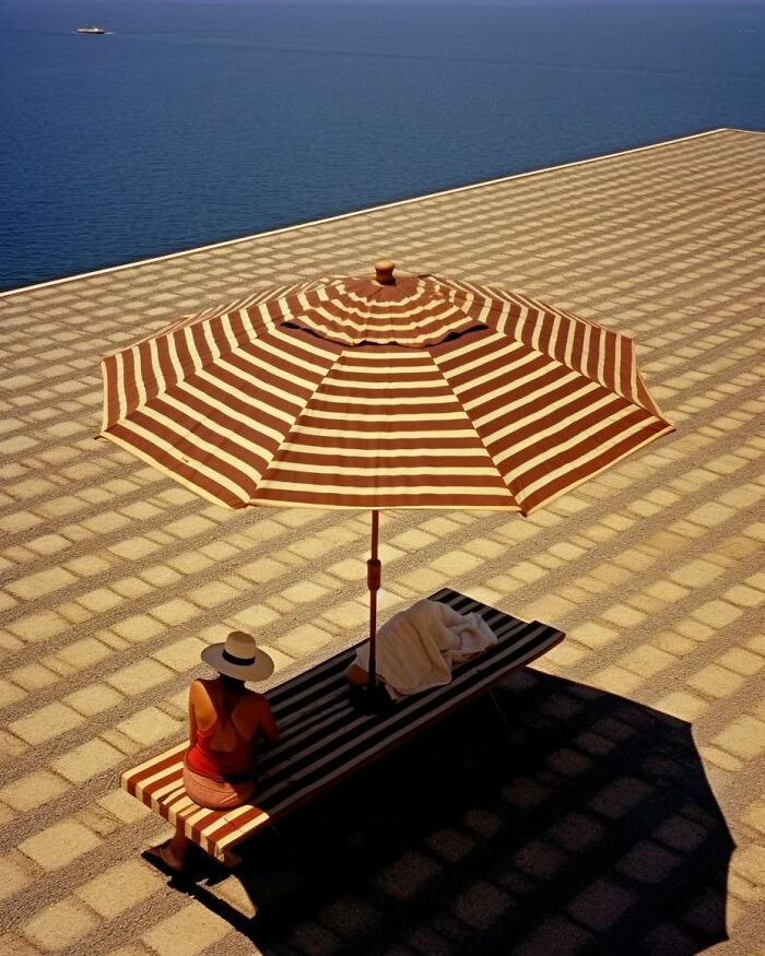 Minimalist photo of a woman sitting under a striped umbrella by the sea, evoking a peaceful escape atmosphere.