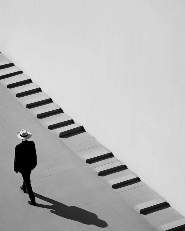 Person walking along minimalist stairs with strong shadows in a dreamy minimalist photo evoking peaceful escape.