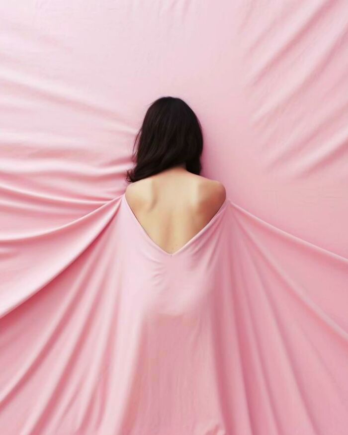 Woman with bare back wrapped in flowing pink fabric, minimalist photo capturing a peaceful and dreamy escape atmosphere.