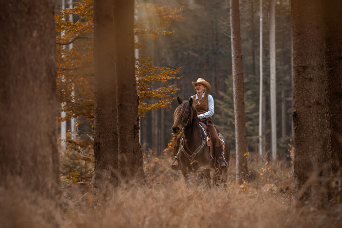 Woman with long blonde hair and tattoos sitting in a field beside a horse in a creative pet photo winning award.