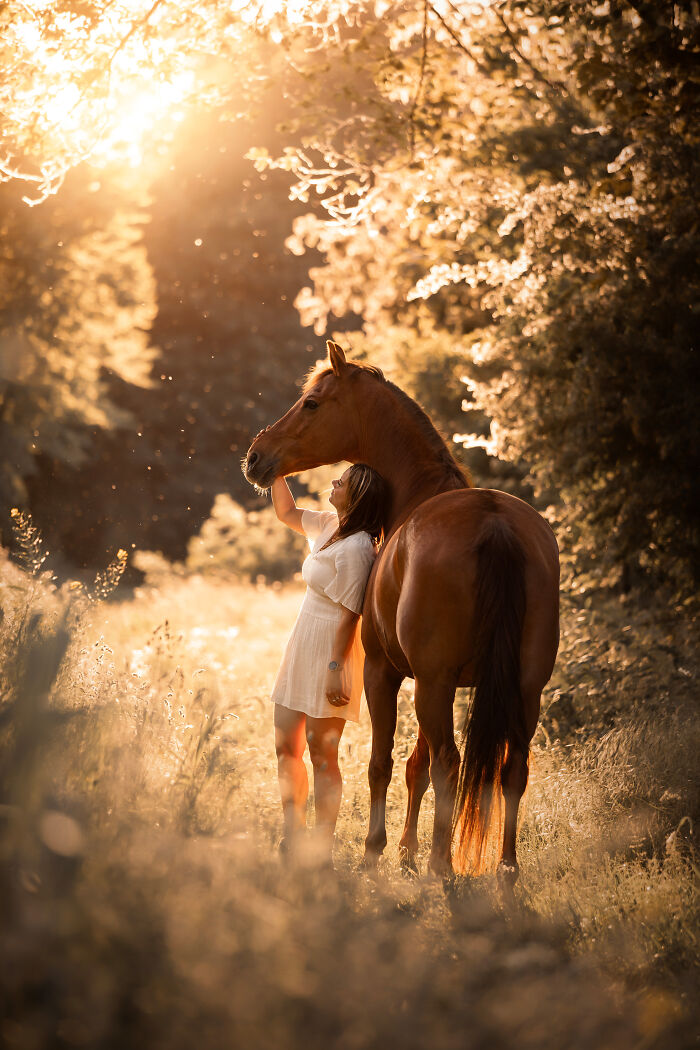 Woman running alongside a rearing horse in a flower-filled field, capturing creative pet photos with heartwarming energy.