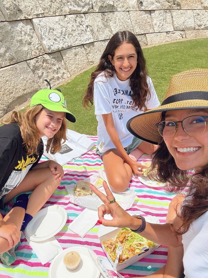 Woman with glasses and hat having a picnic with two children outdoors, related to Bruce Willis' wife defending move amid dementia. Woman with glasses and hat having a picnic with two children outdoors, related to Bruce Willis' wife defending move amid dementia.