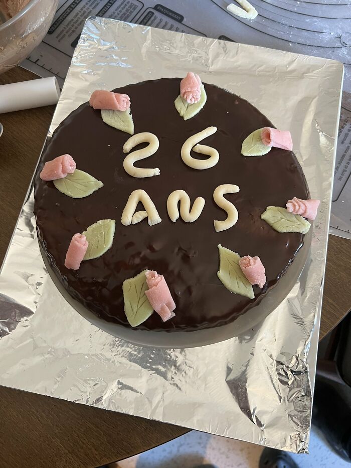 Chocolate cake with pink rose decorations and icing reading 26 ans, capturing wholesome moms happiness moments.