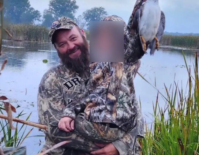 Man and child in camouflage gear by a lake, child holding a bird, related to Michigan church tragedy conspiracy theorists. Man and child in camouflage gear by a lake, child holding a bird, related to Michigan church tragedy conspiracy theorists.