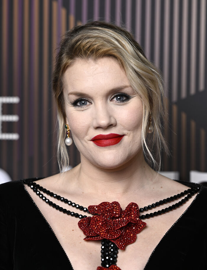 Blonde woman with red lipstick wearing a black dress with red floral embellishment, related to 1800s Wuthering Heights theme. Blonde woman with red lipstick wearing a black dress with red floral embellishment, related to 1800s Wuthering Heights theme.
